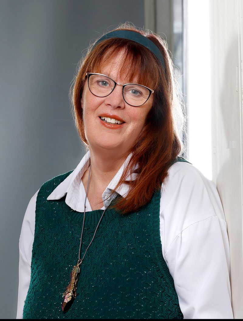 Susanne Schnepel, lächelnd, am Fenster, in grünem Pullunder und weißer Bluse